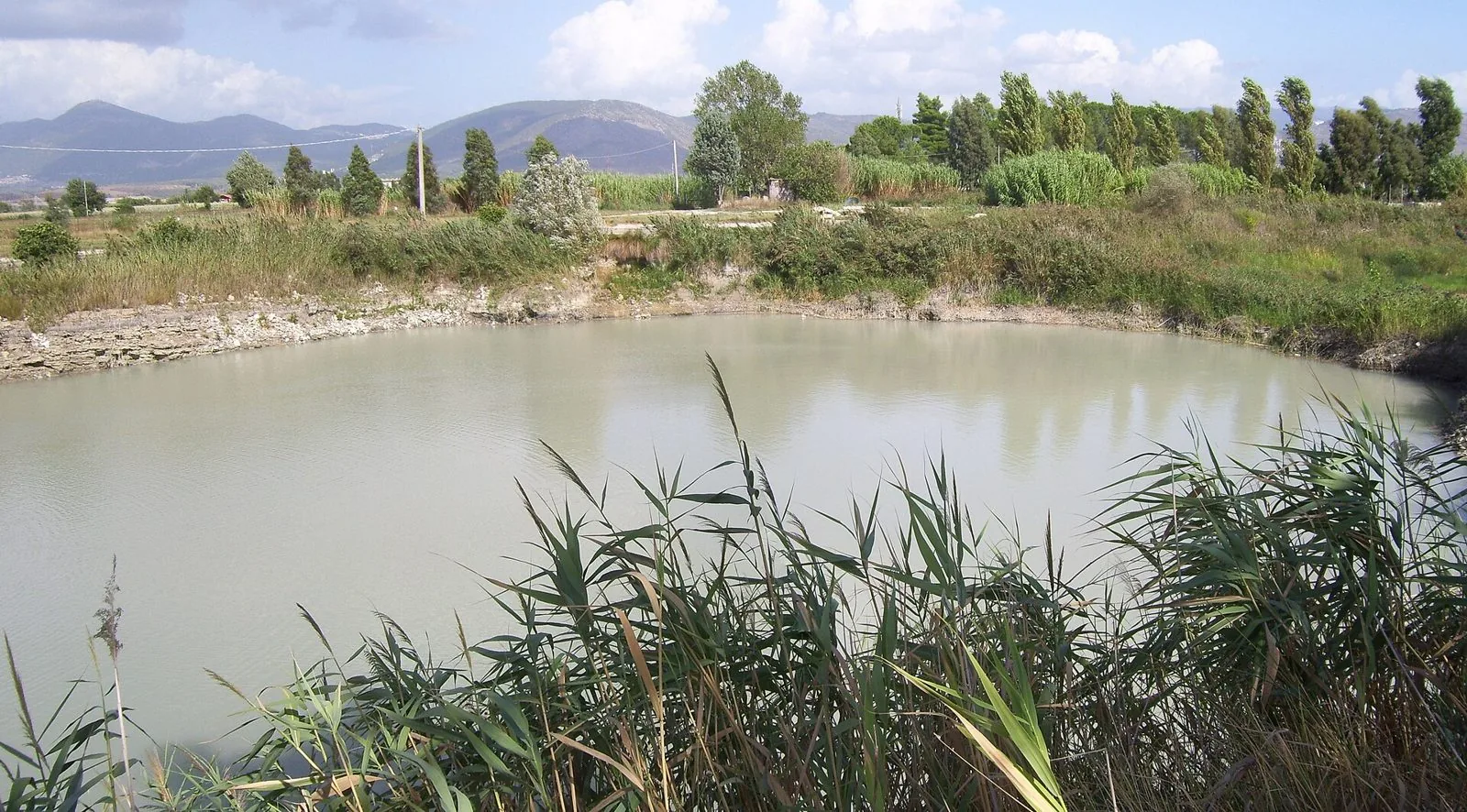 Il Lago della Regina con l'acqua sulfurea di colore lattiginoso, circondato da canneti e alberi, con i monti sullo sfondo