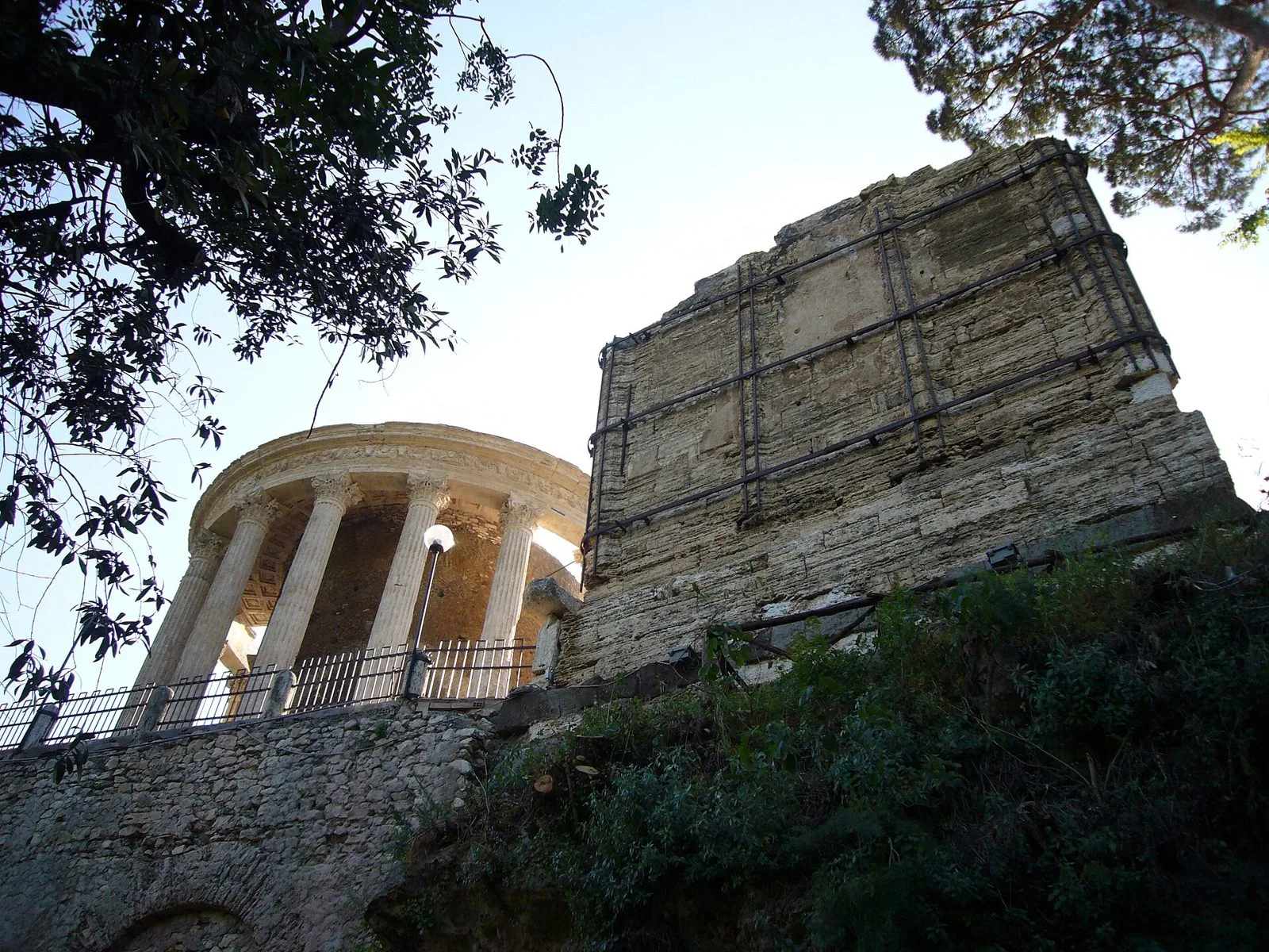 Il Tempio di Vesta a pianta circolare con le colonne corinzie e, accanto, la parete in blocchi di pietra del Tempio della Sibilla visti dal basso tra gli alberi