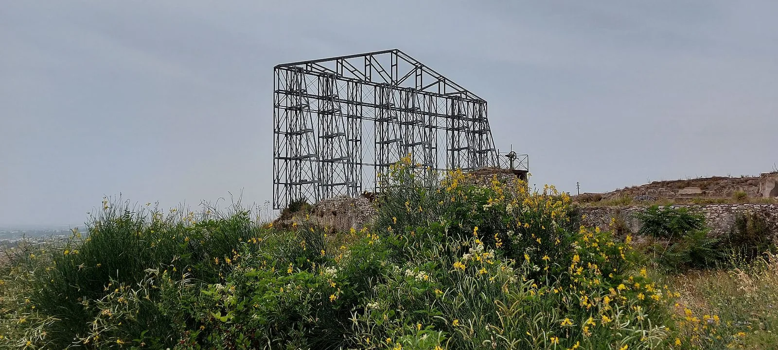 La struttura metallica che evoca il tempio sul podio del Santuario di Ercole Vincitore a Tivoli, tra ginestre in fiore e resti di murature