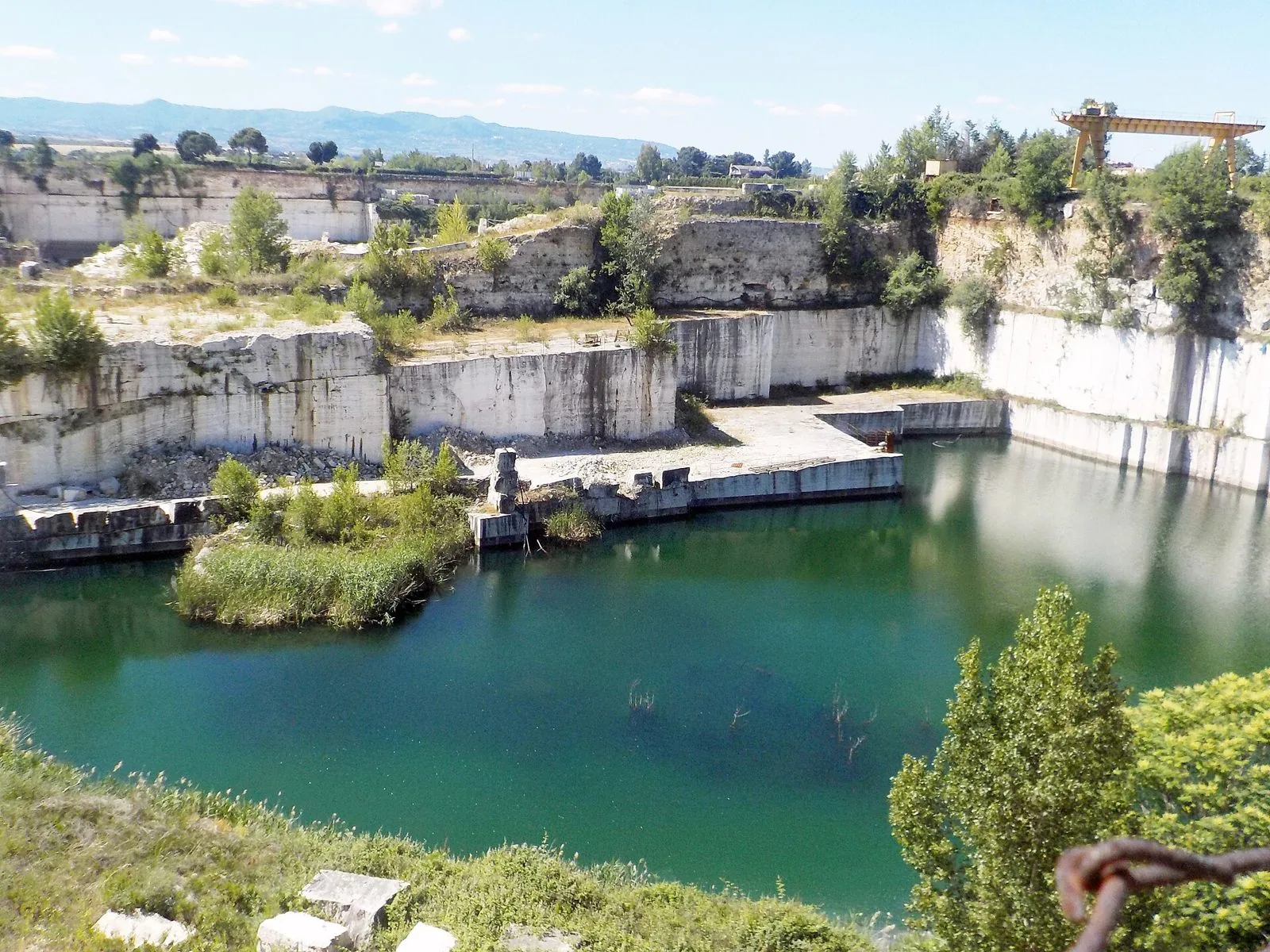 Cava di travertino dismessa con pareti bianche tagliate a gradoni e un laghetto verde smeraldo sul fondo, nella zona delle Acque Albule